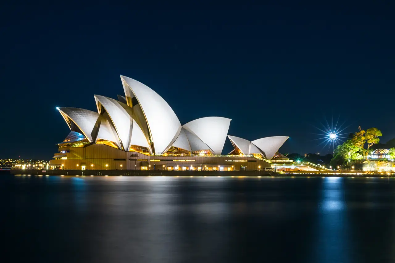 Sydney Opera House illuminated brightly at night across the dark harbor