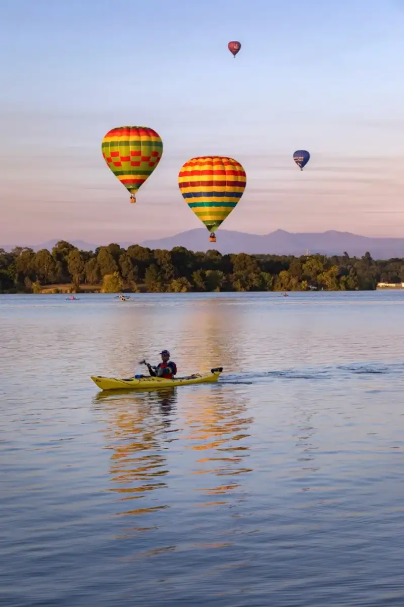 Person kayaking on the lake in Canberra with hot air balloons in the background